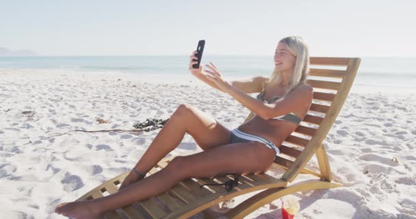 Mulher Caucasiana Desfrutando Tempo Praia Sentada Uma Espreguiçadeira Tirando Uma — Vídeo de Stock