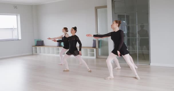4人の白人女性バレエダンサーは 明るいスタジオでバレエクラス中にダンスルーチンを練習し スローモーションで黒の三角形を身に着けています — ストック動画