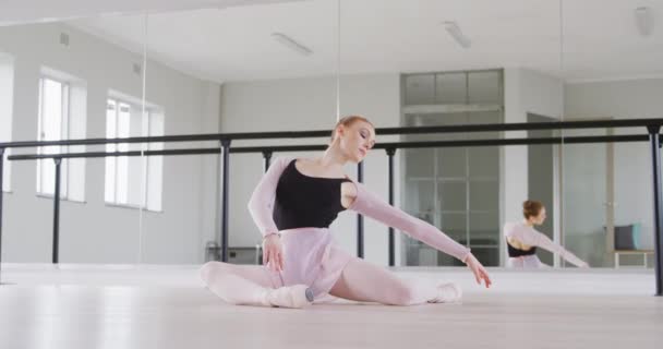 黒の三重奏を身に着けている白人女性バレエダンサー 明るいスタジオでダンスクラスの準備 床にストレッチ スローモーションで — ストック動画