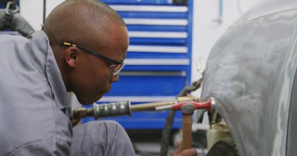 在乡镇车间工作的非裔美国男性汽车修理工 手里拿着螺丝刀 用锤子修理一辆慢动作的汽车 — 图库视频影像