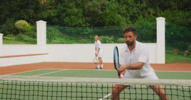 Beyaz tenli, beyaz tenli, beyaz tenli, güneşli bir günde tenis oynayan, tenis raketi tutan, biri yavaş çekimde topa vuran bir beyaz ırk..