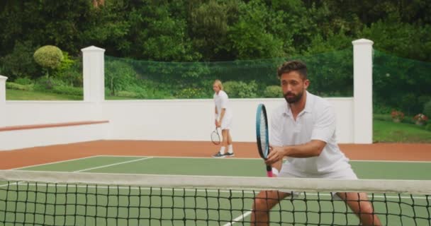 一名白种人和一名混血人 身穿白种人的网球服 在阳光灿烂的日子里一起打网球 拿着网球拍 其中一人慢动作地击球 — 图库视频影像