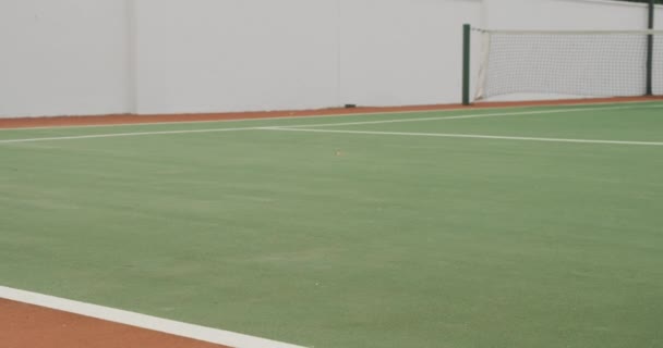 コートに横たわってテニスラケットとテニスボールを保持し 遅い動きで コートに時間を費やして 晴れた日にテニスをして テニスを着て混合レースの男 — ストック動画