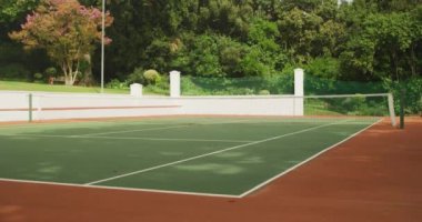 Güneşli bir günde ortasında ağ olan boş bir tenis kortunun genel görüntüsü. Arka planda bir ağacın gölgesi, yavaş çekimde..