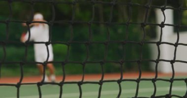 Beyazlar içinde tenis oynayan, güneşli bir günde tenis oynayan, tenis raketi tutan, tenis topuna yavaş çekimde vuran beyaz bir adam..