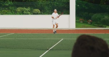 Beyaz tenli, beyaz tenli, beyaz tenli, güneşli bir günde tenis oynayan, tenis raketi tutan, biri yavaş çekimde topa vuran bir beyaz ırk..
