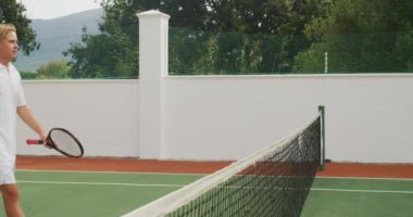 Güneşli bir günde tenis oynayan, el sıkışan ve tenis raketlerini yavaş çekimde tutan beyaz tenisçi ve melez bir ırk..