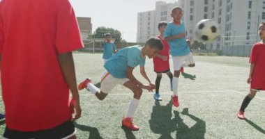 Güneşli bir günde, yeşil bir futbol sahasında futbol oynayan iki çocuk takımından oluşan çok ırklı bir grup.