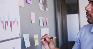 Yaratıcı bir işyerindeki Mixedrace işadamı tahtaya yavaş çekimde yazı yazıyor. İş adamları ve iş arkadaşları yoğun bir kreatif ofiste