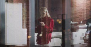 Kafkasyalı iş kadını, akşamları modern bir ofiste ağır çekimde camdan bir tablet kullanarak çalışıyor..