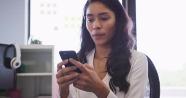 Yaratıcı bir iş yerindeki karışık ırk işkadını akıllı telefon kullanıyor ve gülümsüyor, ağır çekimde. İş adamları ve iş arkadaşları yoğun bir kreatif ofiste.