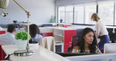 Kafkasyalı bir işadamı, yaratıcı bir iş yerinde sabit bir telefondan ağır çekimde konuşuyor. İş adamları ve iş arkadaşları yoğun bir kreatif ofiste