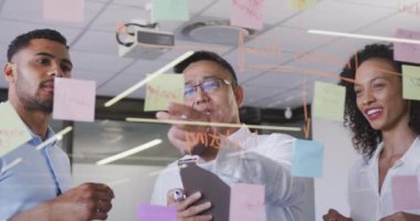 Yaratıcı bir iş yerindeki çok ırklı iş arkadaşları cam duvara bakıyor ve yavaş çekimde konuşuyorlar. İş adamları ve iş arkadaşları yoğun bir kreatif ofiste.