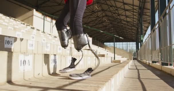 スタンドで彼の足をチェック屋外スポーツ競技場で義肢の脚を持つ障害者混合レース男性選手の低セクション スローモーションで — ストック動画