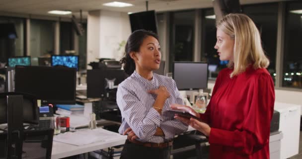 現代のオフィスで夜遅くに働いている白人とアジアのビジネスマンの女性は 握手を交わし 笑顔で スローモーションでプロジェクトを議論するデジタルタブレットを使用しています — ストック動画