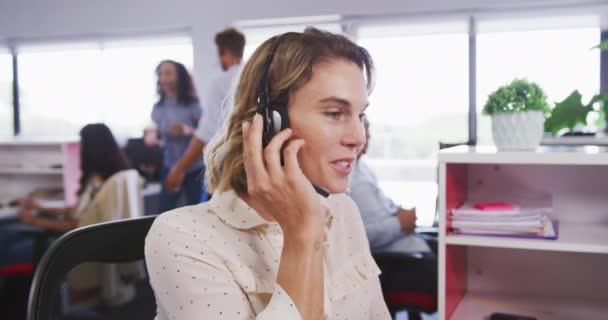 Καυκάσια Επιχειρηματίας Στο Γραφείο Μιας Δημιουργικής Επιχείρησης Φορώντας Ακουστικά Τηλεφώνου — Αρχείο Βίντεο