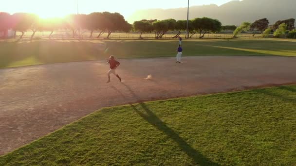 在阳光明媚的一天 一个棒球队的队员在外面的棒球场上打一场比赛 这名击球手跑着回到了主场 被无人驾驶飞机击中 — 图库视频影像