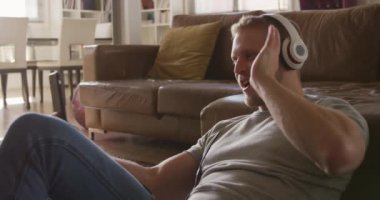 Kafkasyalı bir adam oturma odasında yerde oturmuş kulaklık takıyor, akıllı telefondan video görüşmesi yapıyor ve el sallıyor, ağır çekimde. Karantina karantinasında sosyal uzaklık ve kişisel izolasyon