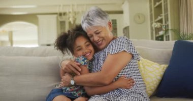 Kıdemli Afro-Amerikan kadın ve torunu evde birlikte vakit geçiriyorlar, oturma odasında bir kanepede oturuyorlar, sarılıyorlar ve gülümsüyorlar, ağır çekimde..
