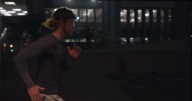 Akşamları şehir parkında spor yapan, farları açık bir şekilde hızla koşan genç bir beyaz adam. Sağlıklı kentsel aktif yaşam biçimi.