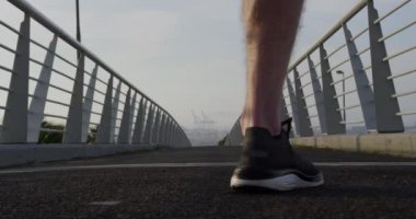 Genç bir atletik beyaz adam bir şehirde yaya köprüsünde egzersiz yapıyor, ağır çekimde çok hızlı koşuyor. Sağlıklı kentsel aktif yaşam biçimi.