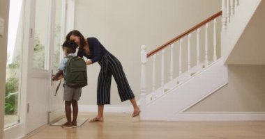 Afrikalı Amerikalı kadın ve oğlu salonda durup okula gitmeden önce yavaş çekimde vedalaşıyorlar..