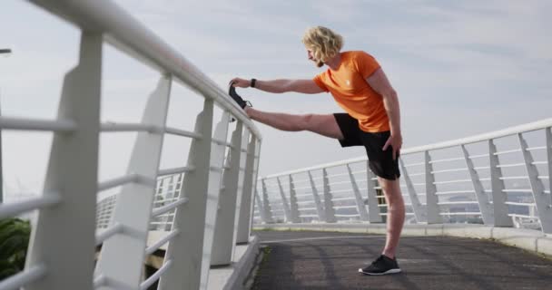 Молодой Атлетичный Кавказский Мужчина Тренируется Пешеходном Мосту Городе Растягивая Ногу — стоковое видео