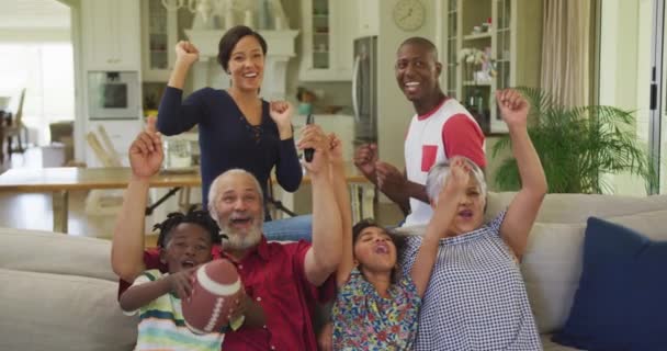 6人のアフリカ系アメリカ人の家族が家で一緒に時間を過ごしリビングでソファに座りテレビを見て歓声を上げ手を上げてゆっくりと動き — ストック動画
