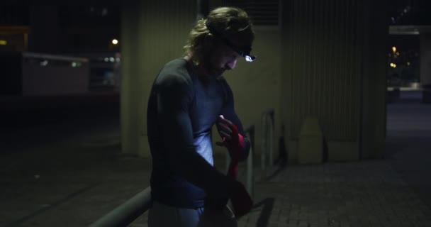 傍晚时分 一个年轻的运动白人男子在一个城市公园里锻炼 用前灯捂住双手 健康的城市生活方式 — 图库视频影像