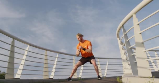 市内の歩道橋で運動をしている若い運動選手の白人男性は ゆっくりと運動をしている 健康的な都市生活 — ストック動画
