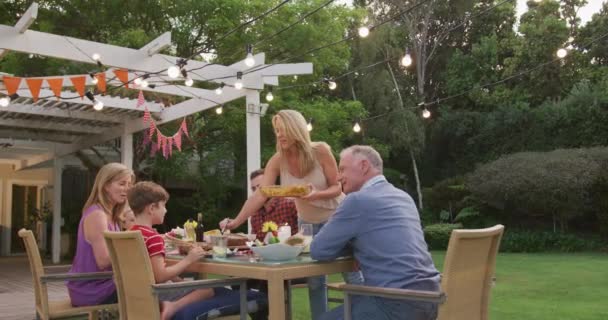 多代白人家庭一起呆在花园里 坐在餐桌旁 慢吞吞地把食物放在盘子里 — 图库视频影像