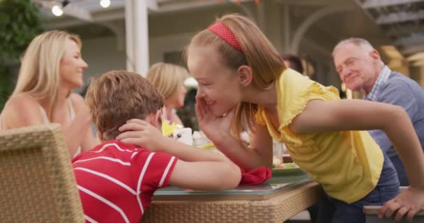 一代又一代的白人家庭一起呆在花园里 坐在餐桌旁 一边吃饭一边说话 这个女孩慢吞吞地在她哥哥的耳边窃窃私语 — 图库视频影像