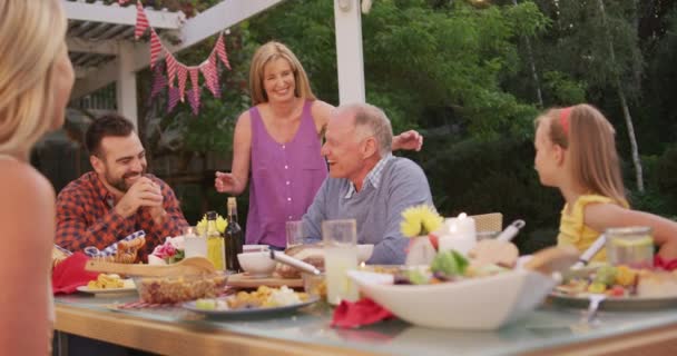 几代白人家庭一起在花园度过时光 坐在餐桌前 年长的女人慢吞吞地亲吻着她的丈夫 — 图库视频影像