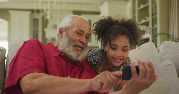 老非洲裔美国人和他的孙女一起呆在家里 坐在客厅的沙发上 用智能手机 动作缓慢 — 图库视频影像