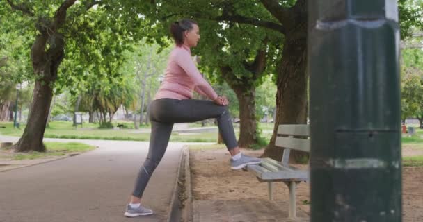 スポーツウェアを着て公園で働くシニアフィット白人女性は スローモーションでベンチに足を伸ばします 退職健康的なライフスタイル活動 — ストック動画