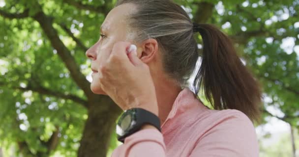 高体格的白人女人穿着运动服在公园里锻炼 慢慢地戴上耳机 退休后健康生活方式活动 — 图库视频影像
