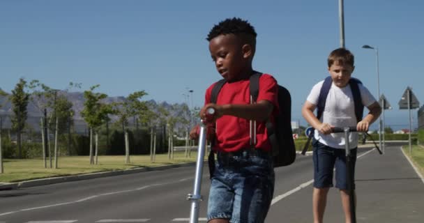 Niños Caucásicos Afroamericanos Montando Scooters Cruzando Calle Llevando Sus Mochilas — Vídeo de stock