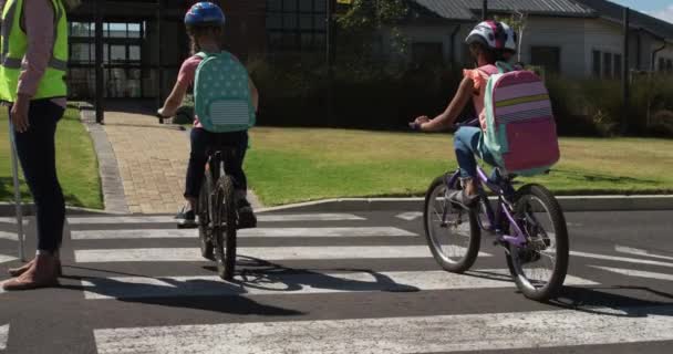 Niñas Afroamericanas Caucásicas Montando Bicicletas Cruzando Calle Llevando Sus Mochilas — Vídeo de stock