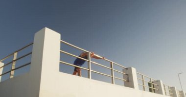 Kıdemli beyaz adam deniz kenarında spor kıyafetleri giyerek gezinti yapıyor, mola veriyor ve yavaş çekimde esniyor. Emeklilik sağlıklı yaşam tarzı aktivitesi.