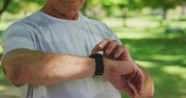 Kıdemli beyaz adam parkta spor kıyafetleriyle çalışıyor, yavaş çekimde koşmadan önce akıllı telefonunu kontrol ediyor. Emeklilik sağlıklı yaşam tarzı aktivitesi.