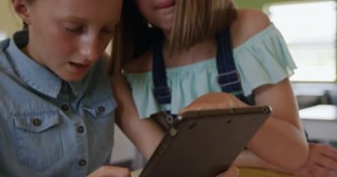 Sınıfta masa başında oturan beyaz kızlar, ağır çekimde tablet bilgisayar kullanıyorlar. İlkokulda eğitim.