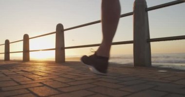 Kıdemli beyaz adam deniz kenarındaki gezinti güvertesinde spor kıyafetleriyle çalışıyor, güneşli bir günde ağır çekimde koşuyor. Emeklilik sağlıklı yaşam tarzı aktivitesi.