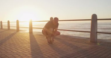 Kıdemli beyaz adam deniz kenarında spor kıyafetleri giyerek, eğilip bağcıklarını bağlayarak ağır çekimde koşmaya başladı. Emeklilik sağlıklı yaşam tarzı aktivitesi.