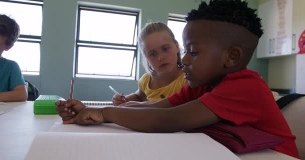在课堂上 一群多种族的孩子坐在教室里 慢吞吞地写在笔记本上 小学的教育 — 图库视频影像