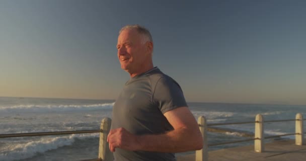高个子白人穿着运动服在海边散步 在阳光灿烂的日子慢吞吞地跑步 退休后健康生活方式活动 — 图库视频影像