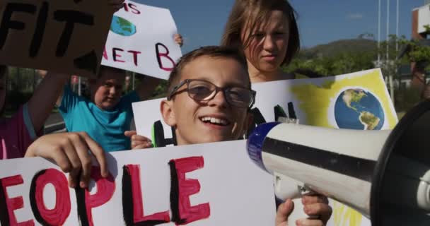 一个混血儿拿着扩音器的画像 看着摄像机 孩子们背着带有环保标语的标志 动作缓慢 小学生生态意识抗议 — 图库视频影像