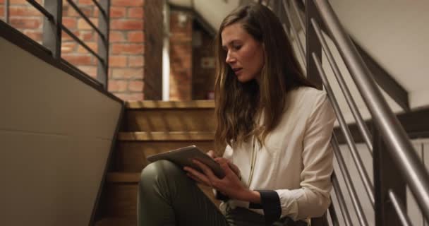 Femme d'affaires professionnelle caucasienne travaillant dans un bureau moderne utilisant une tablette numérique, assise sur un escalier, souriant. Technologie de créativité des entreprises.