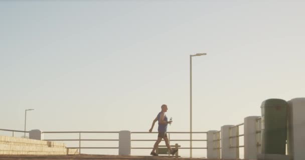 シニアフィットの白人男性は スポーツ服を着て海の遊歩道に取り組み 休憩を取り スローモーションでストレッチを開始します 退職健康的なライフスタイル活動 — ストック動画