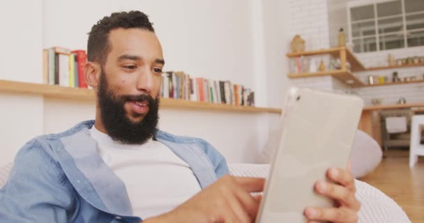 这位混血男子在家里休息 坐在豆袋上 微笑着 并使用数码平板电脑 — 图库视频影像