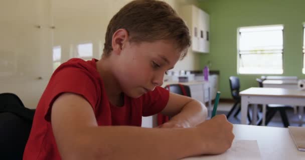 教室の机に座っている白人の少年は ゆっくりとした動きでノートに書いている 小学校での教育 — ストック動画
